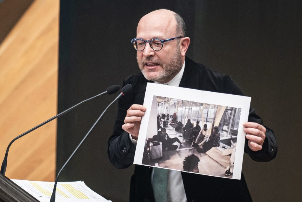 El delegado de Políticas Sociales, Familia e Igualdad en el Ayuntamiento de Madrid, José Fernández Sánchez, sosteniendo una imagen de migrantes asignados en Barajas en el pleno del Ayuntamiento de Madrid.