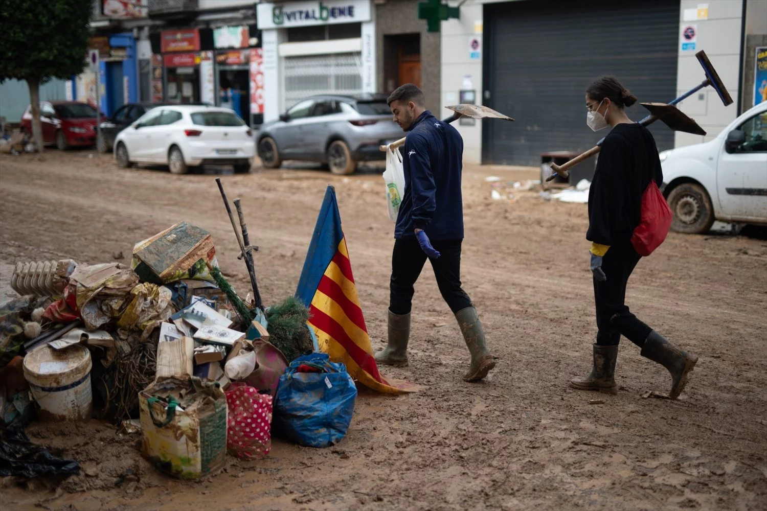 Dos personas con palas observan una bandera de la Comunidad Valenciana mientras pasan por una calle de Benetússer, a 4 de noviembre de 2024, tras la DANA en Benetússer, Valencia, Comunidad Valenciana (España)